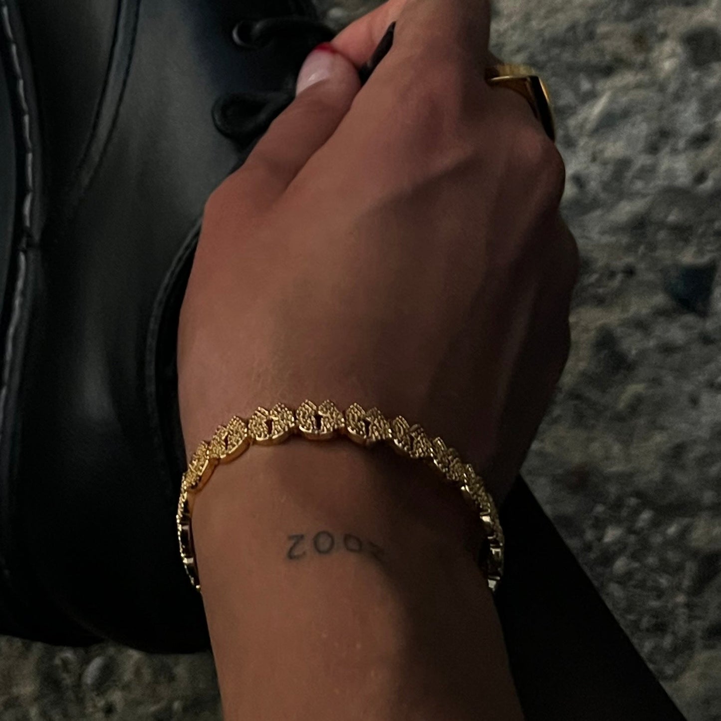 Hand wearing a gold butterfly design bracelet with a white zirconia crust, with a tattoo on the wrist, holding a black boot.