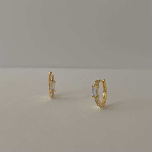 Gold hoop earrings with clear rectangular gemstones and a pave crust, on a gray background