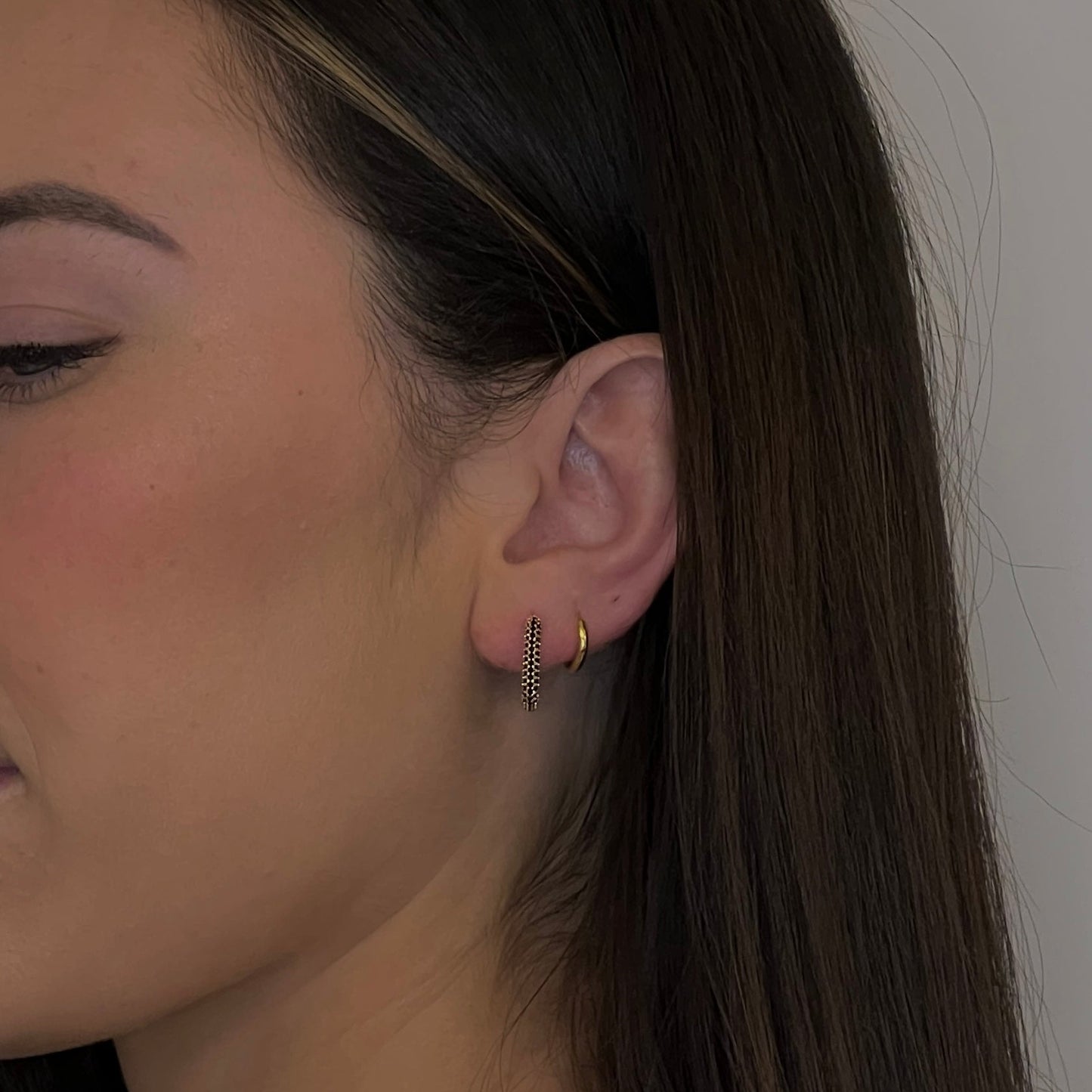 close up of a woman wearing gold rectangular stone earrings with a black zirconia crust