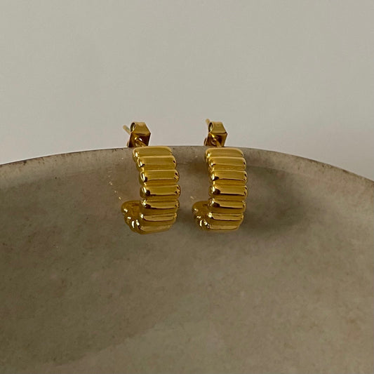 Gold ribbed hoop earrings on a textured surface with a neutral background