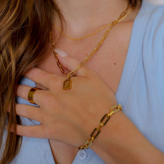 A close up of a woman wearing a gold paperclip chain necklace with a polished gold pendant with a heard motif.