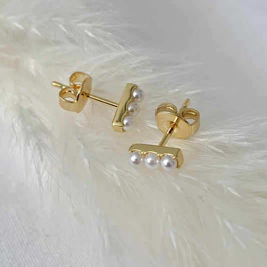 Gold earrings with three pearls on a white feather background