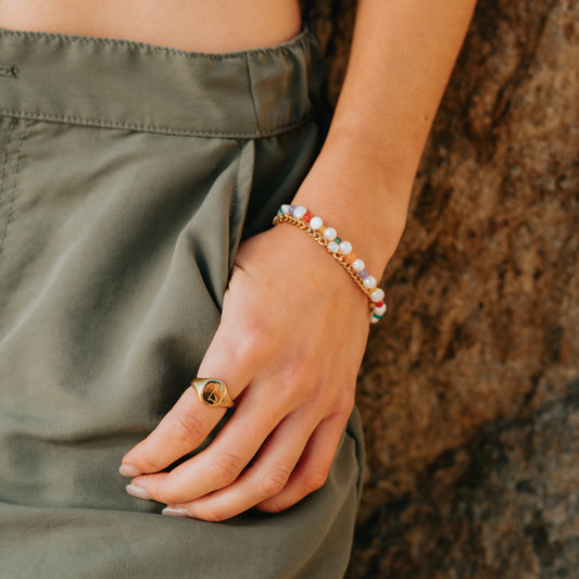Hand wearing a gold ring from daurielle and pearl bracelet against a textured brown background