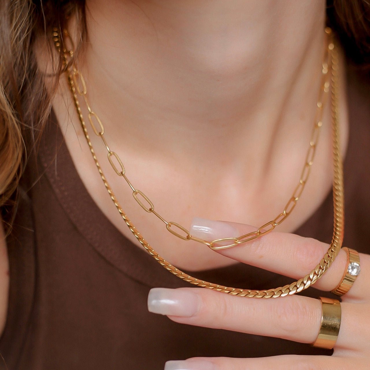 Gold chain necklace being worn with a close-up of the neck and hand.