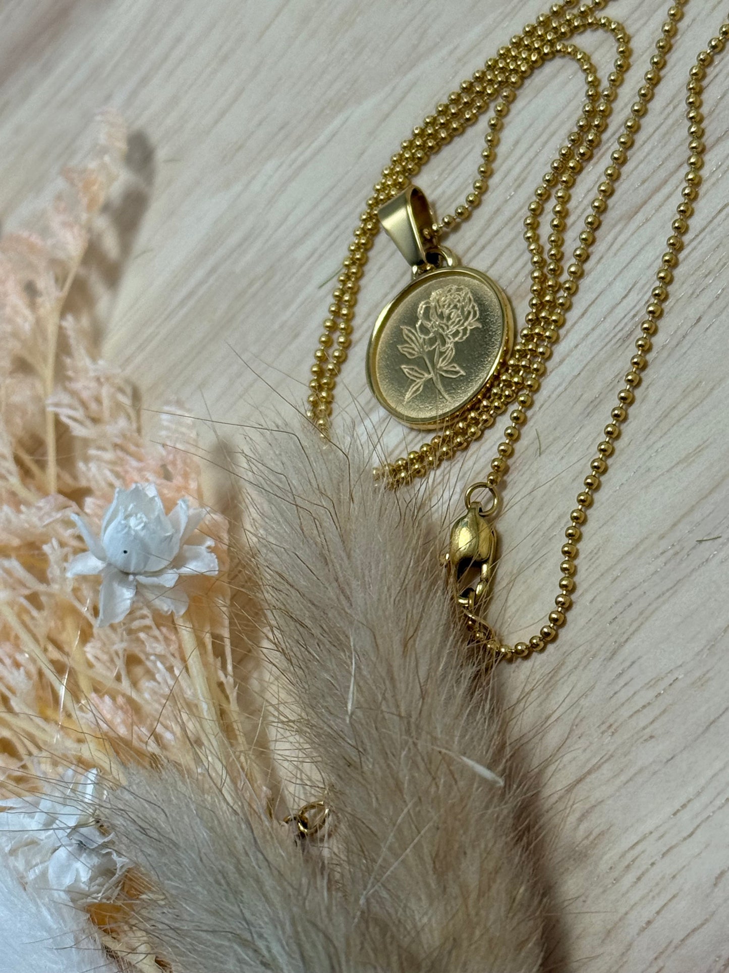Gold necklace with a floral pendant on a textured surface with dried flowers.