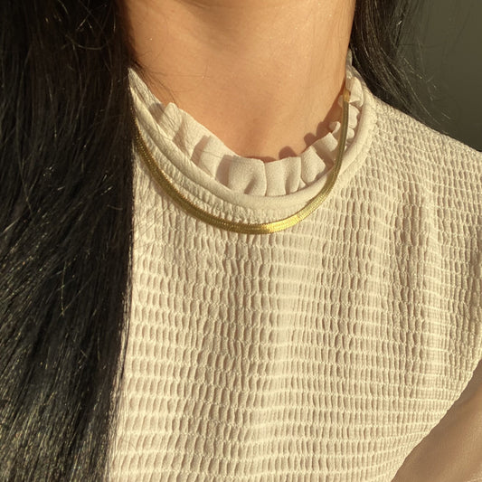 Close-up of a person wearing a textured beige top with a gold herringbone necklace.