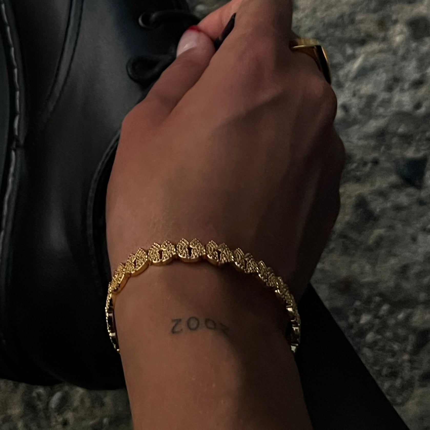 Hand wearing a gold butterfly design bracelet with a white zirconia crust,  with a tattoo on the wrist, holding a black boot.