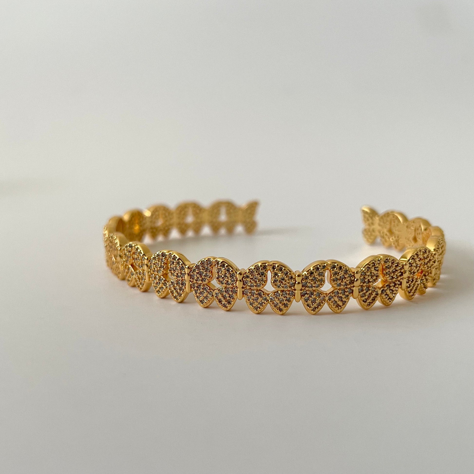 Gold butterfly designed bracelet with white zirconia pave crust,  on a light gray background