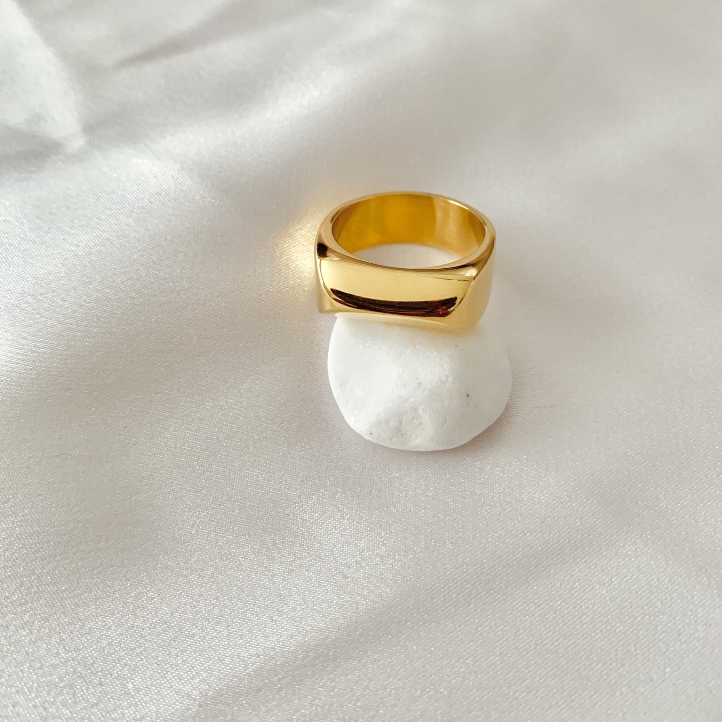 Gold ring on a white stone with a white fabric background