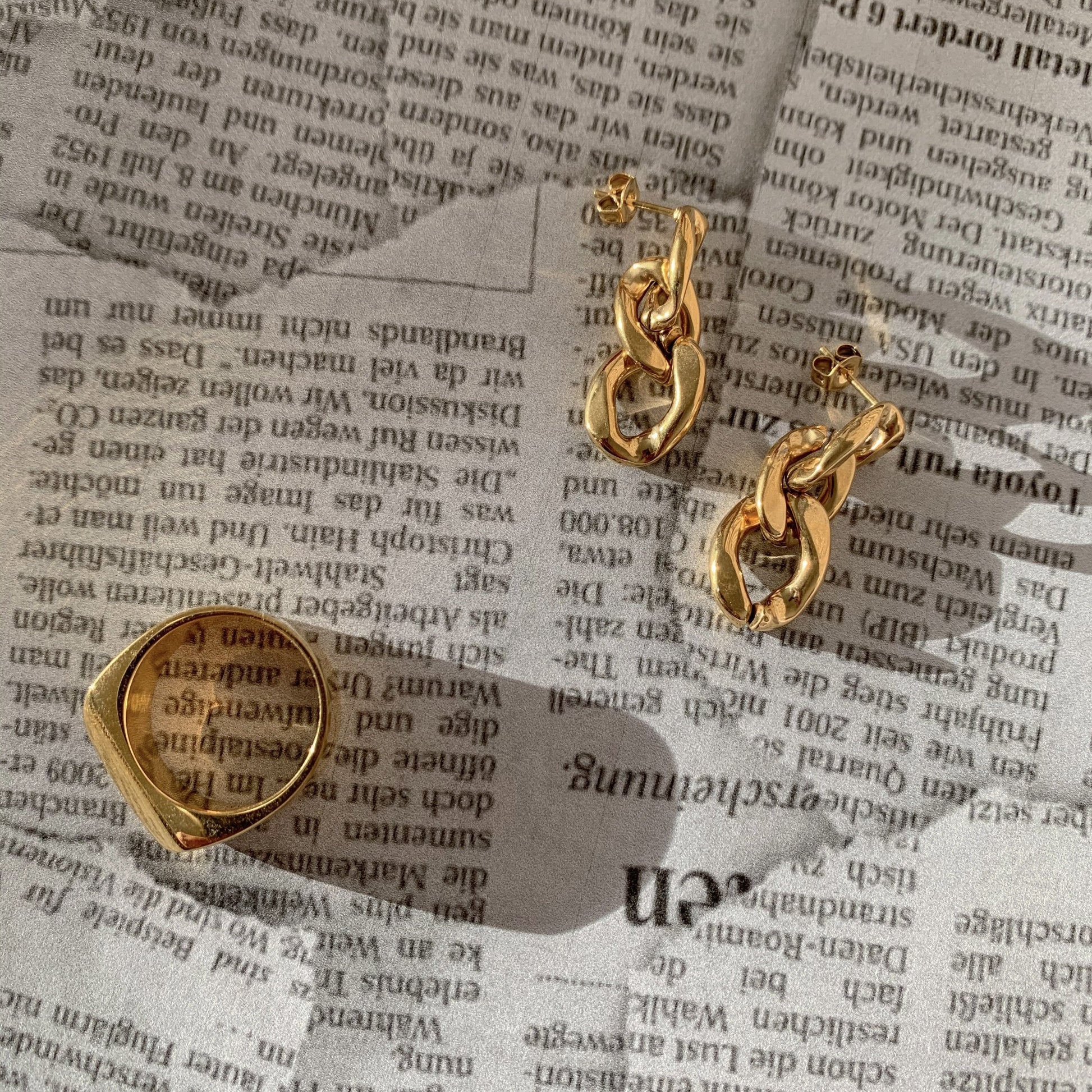 Gold chain earrings next to a gold ring  on a newspaper background