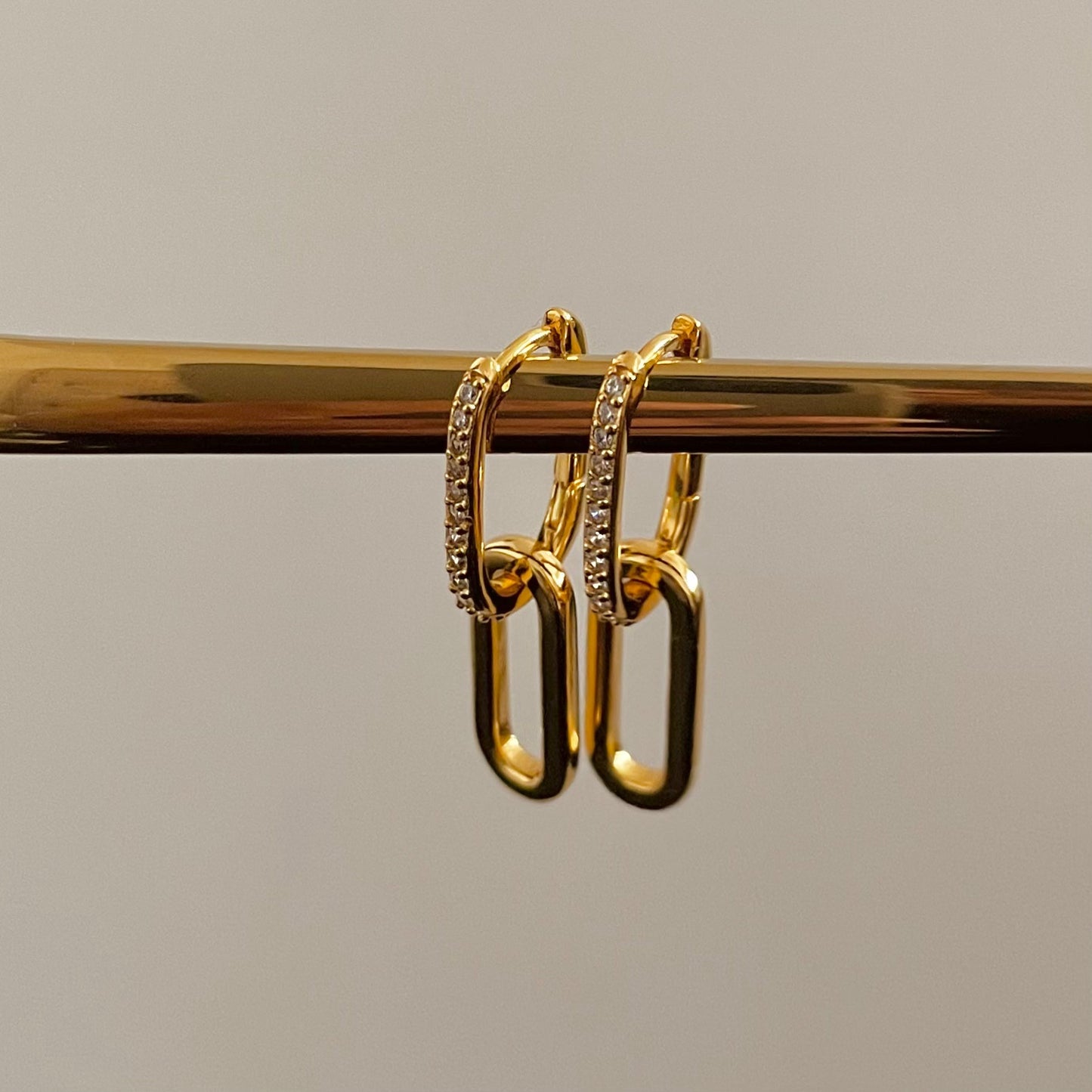 Gold, white zirconia crusted rectangular hoops with gold paperclip style drops on a gold rod, plain grey background