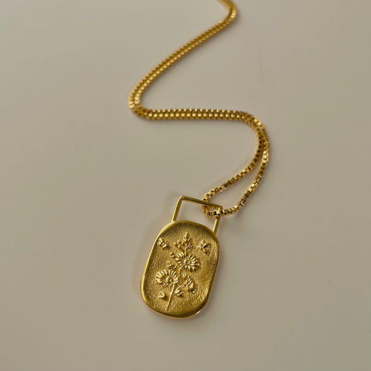 Gold necklace with a pendant featuring floral design on a beige background