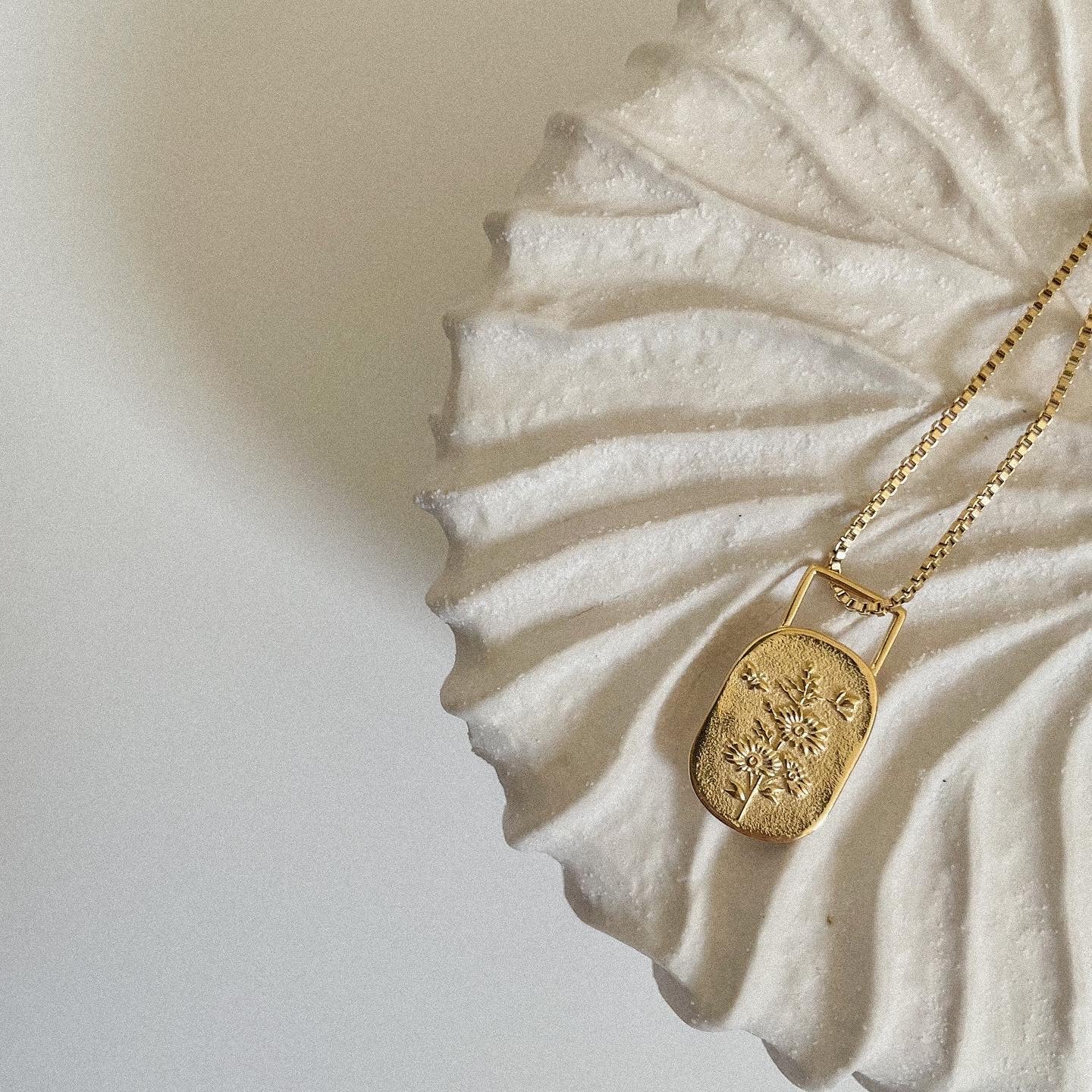 Gold necklace with a floral decorative pendant on a white shell