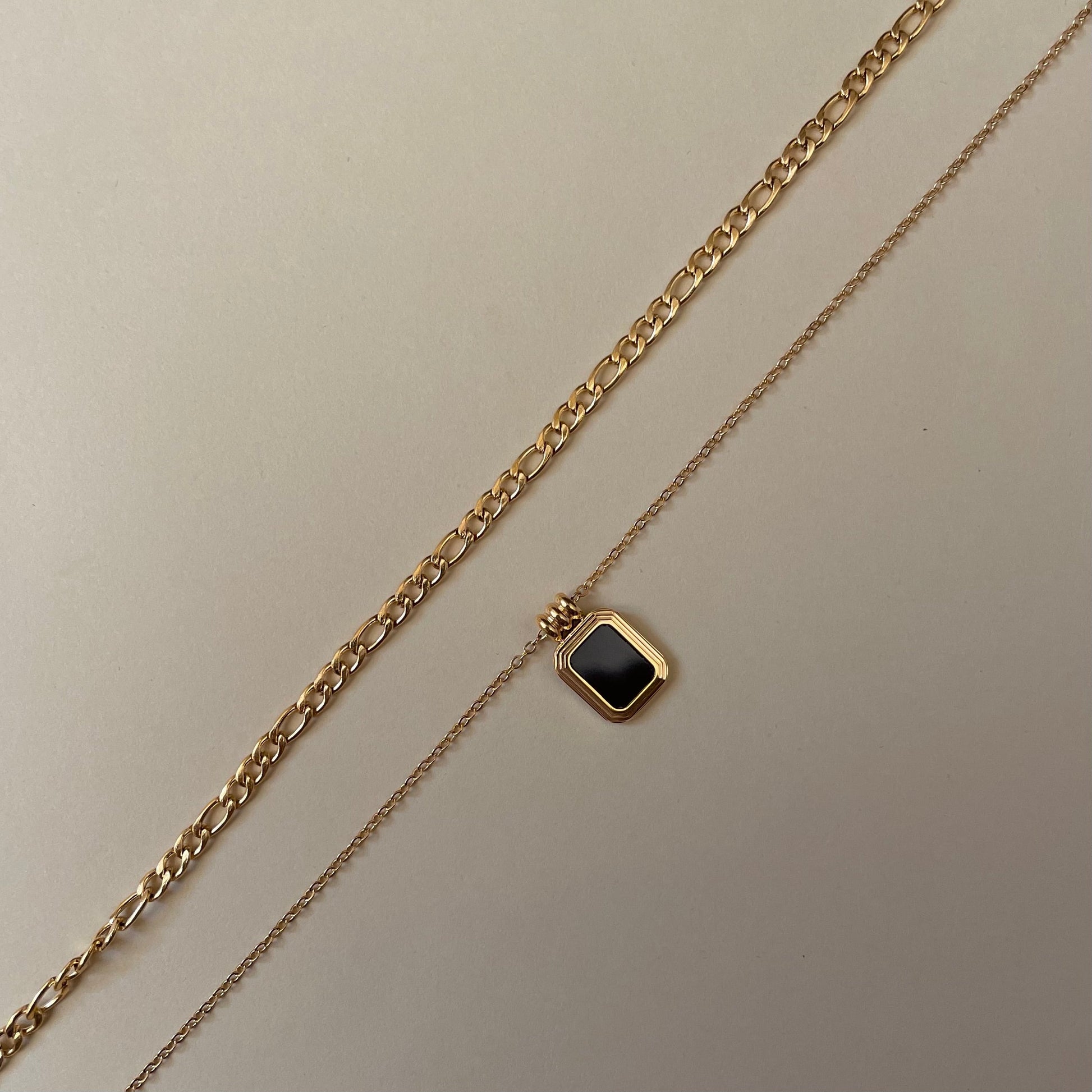  layered Gold chain necklace with a gold square pendant with a black square stone on a beige background
