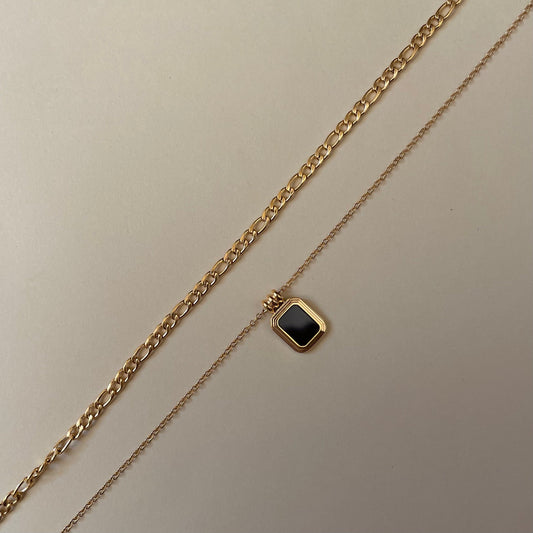  layered Gold chain necklace with a gold square pendant with a black square stone on a beige background