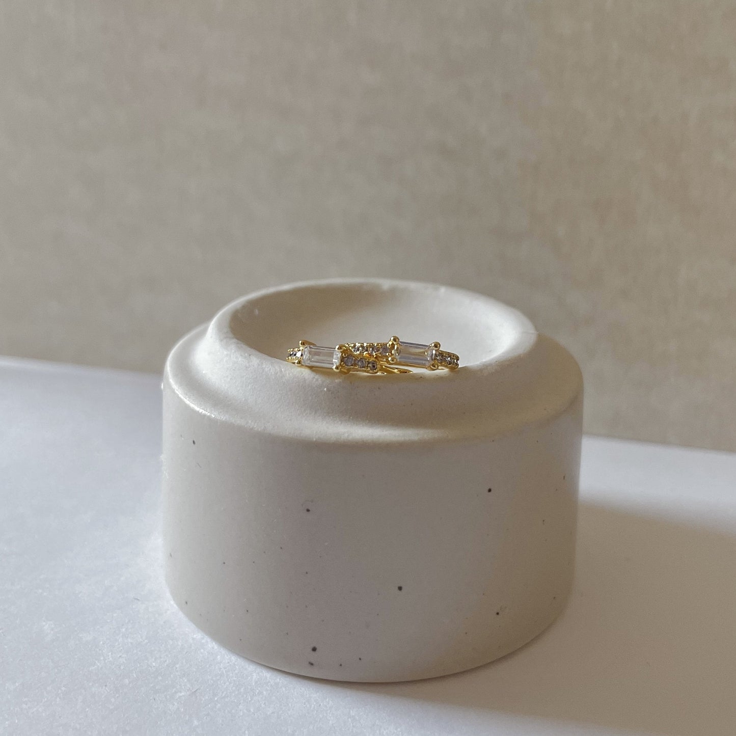 Gold and silver earring set on a white ceramic stand against a neutral background