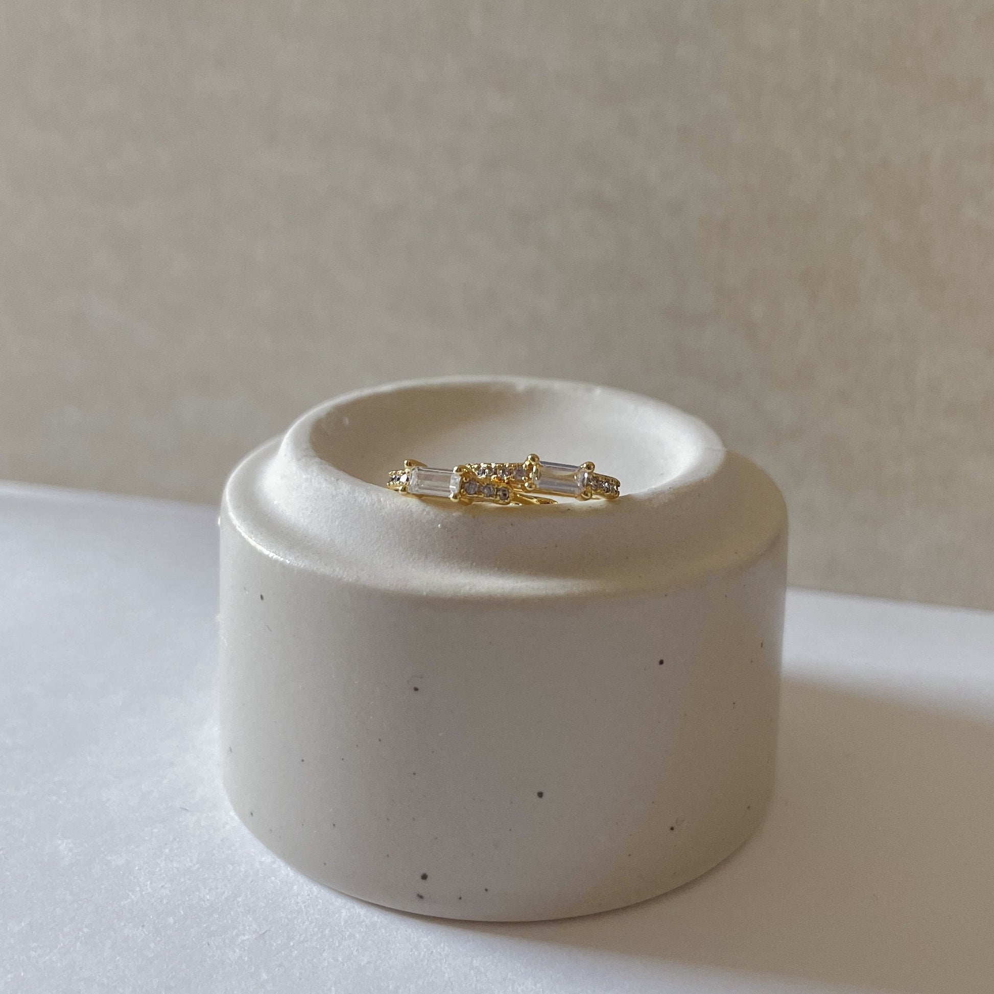 Gold and silver earring set on a white ceramic stand against a neutral background