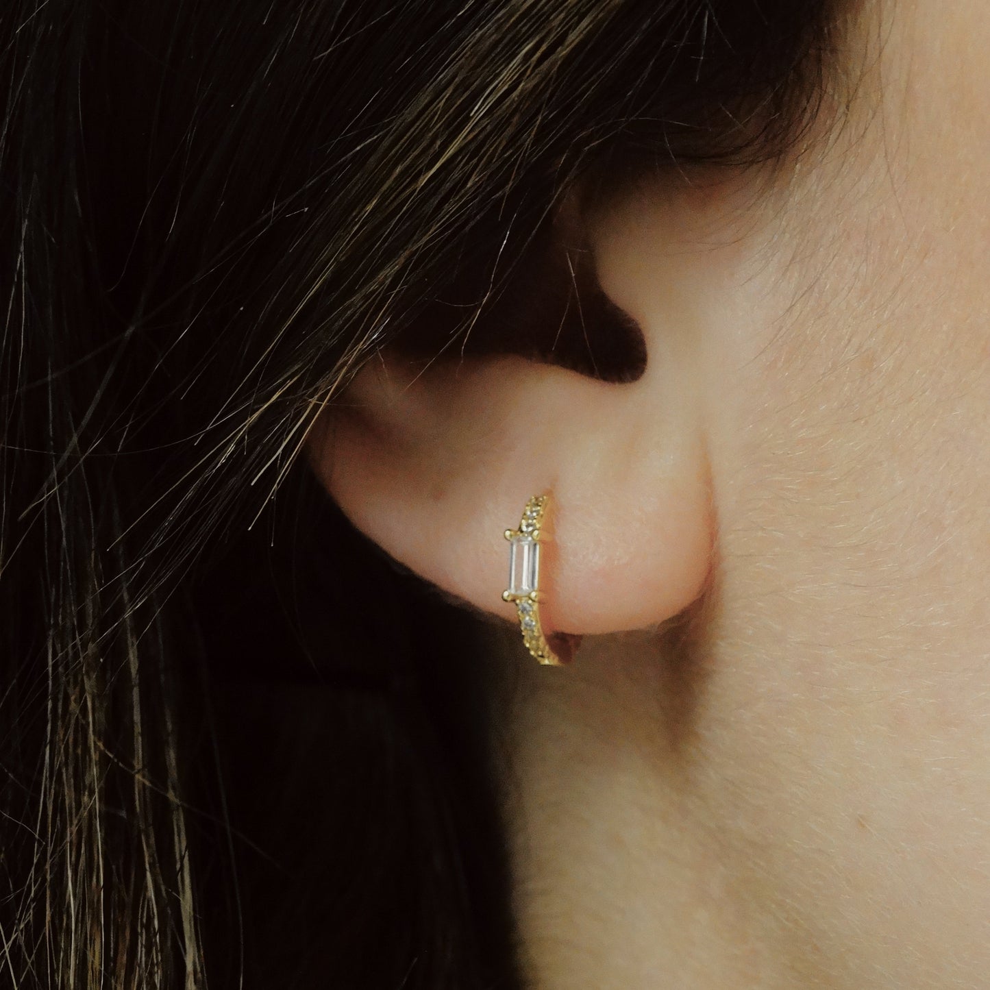 close up of a gold earring with a pave crust and a rectangular white zirconia.