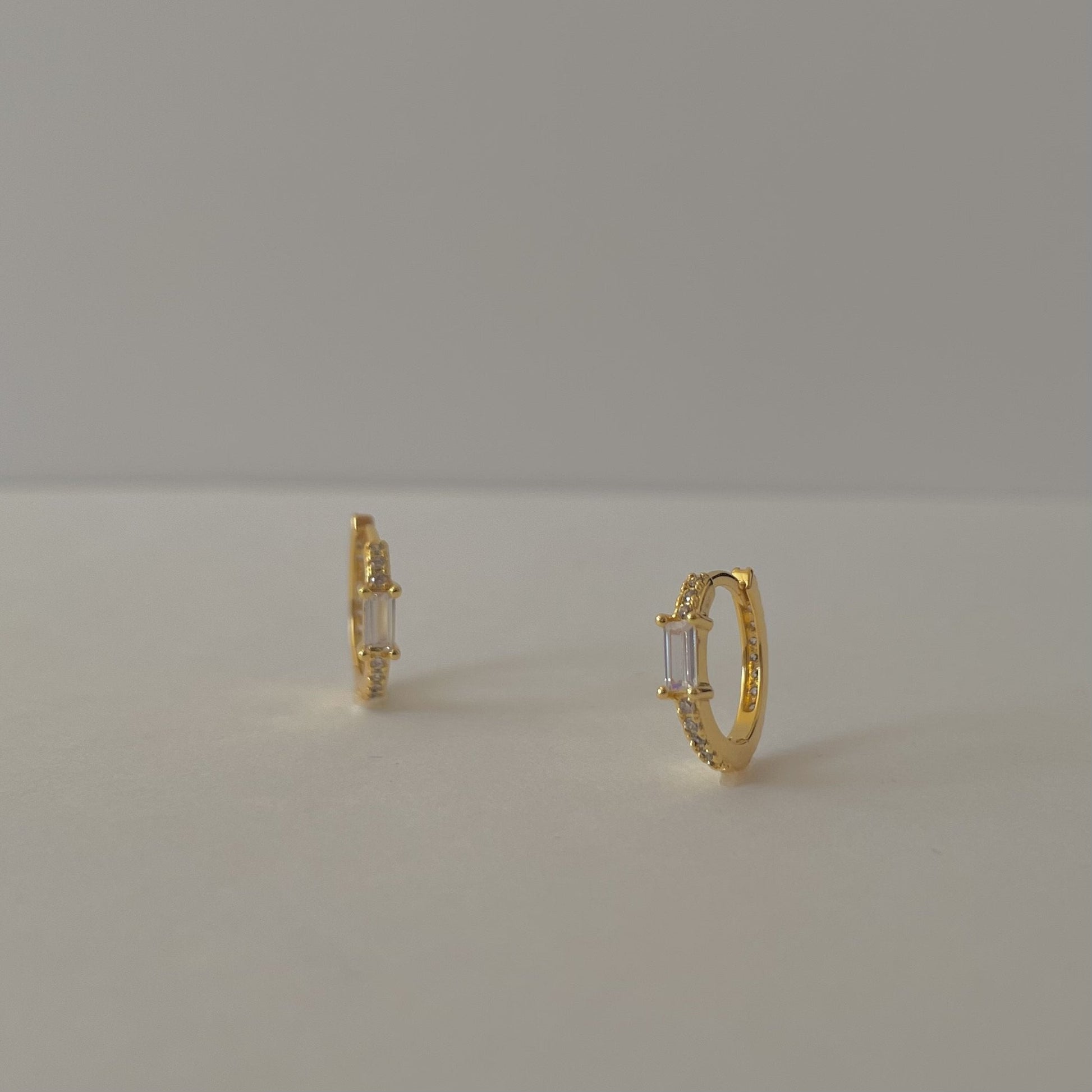 Gold hoop earrings with clear rectangular gemstones and a pave crust, on a gray background