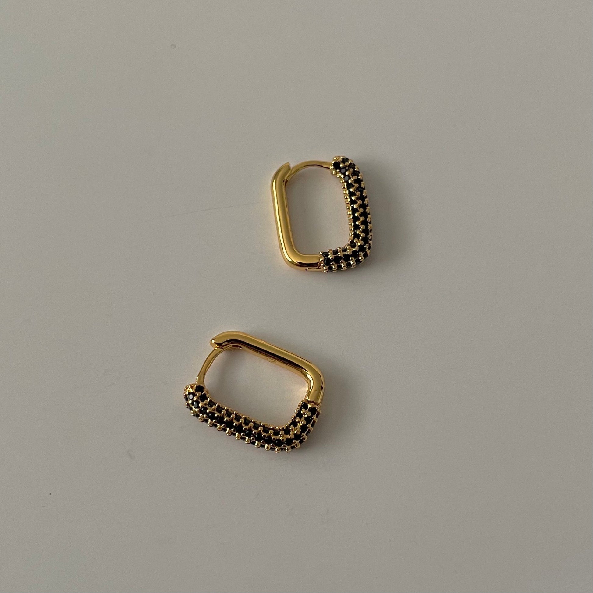 Pair of gold rectangular hoop earrings with black zirconia crust  on a gray background