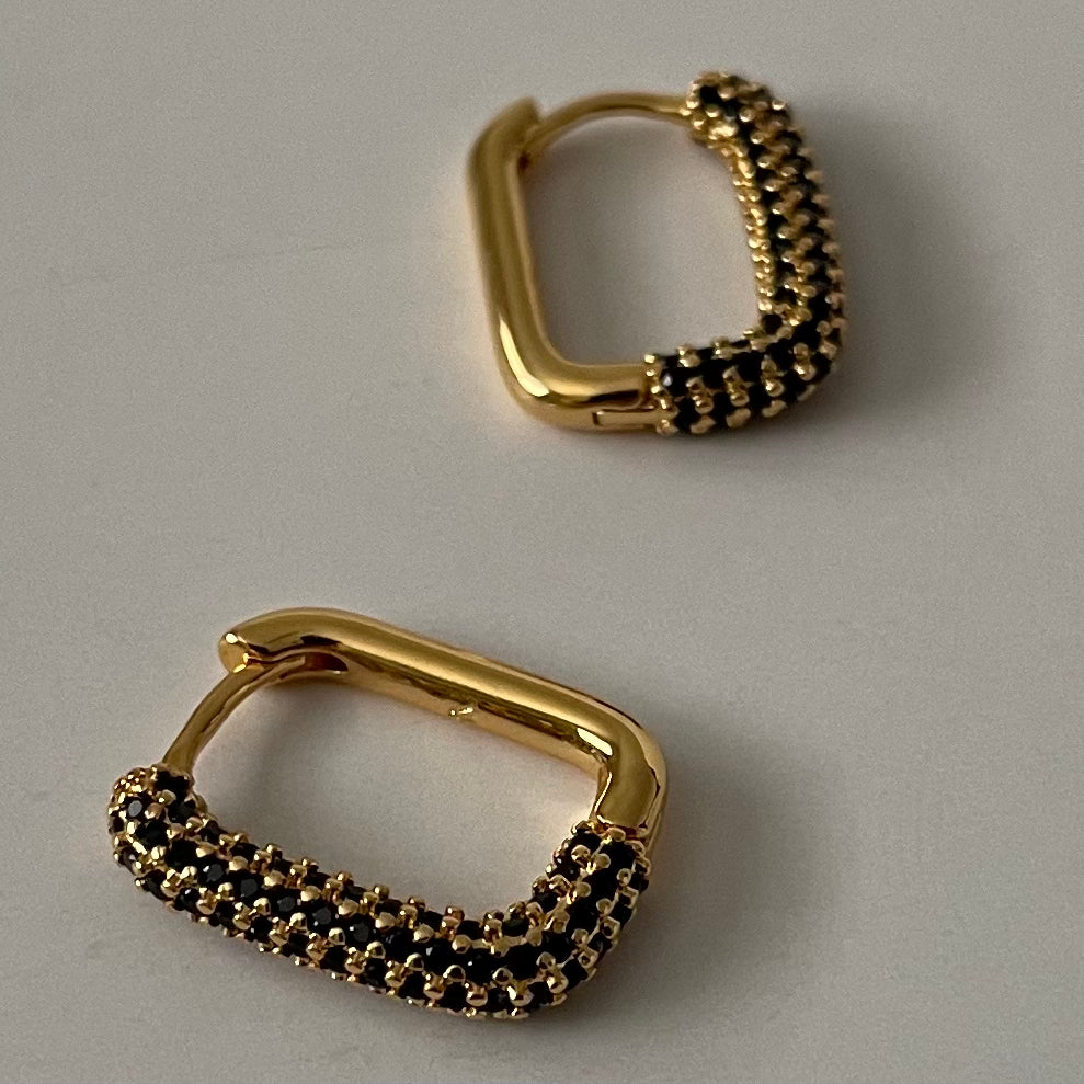 Pair of gold rectangular hoop earrings with black zirconia crust detailing on a light gray background