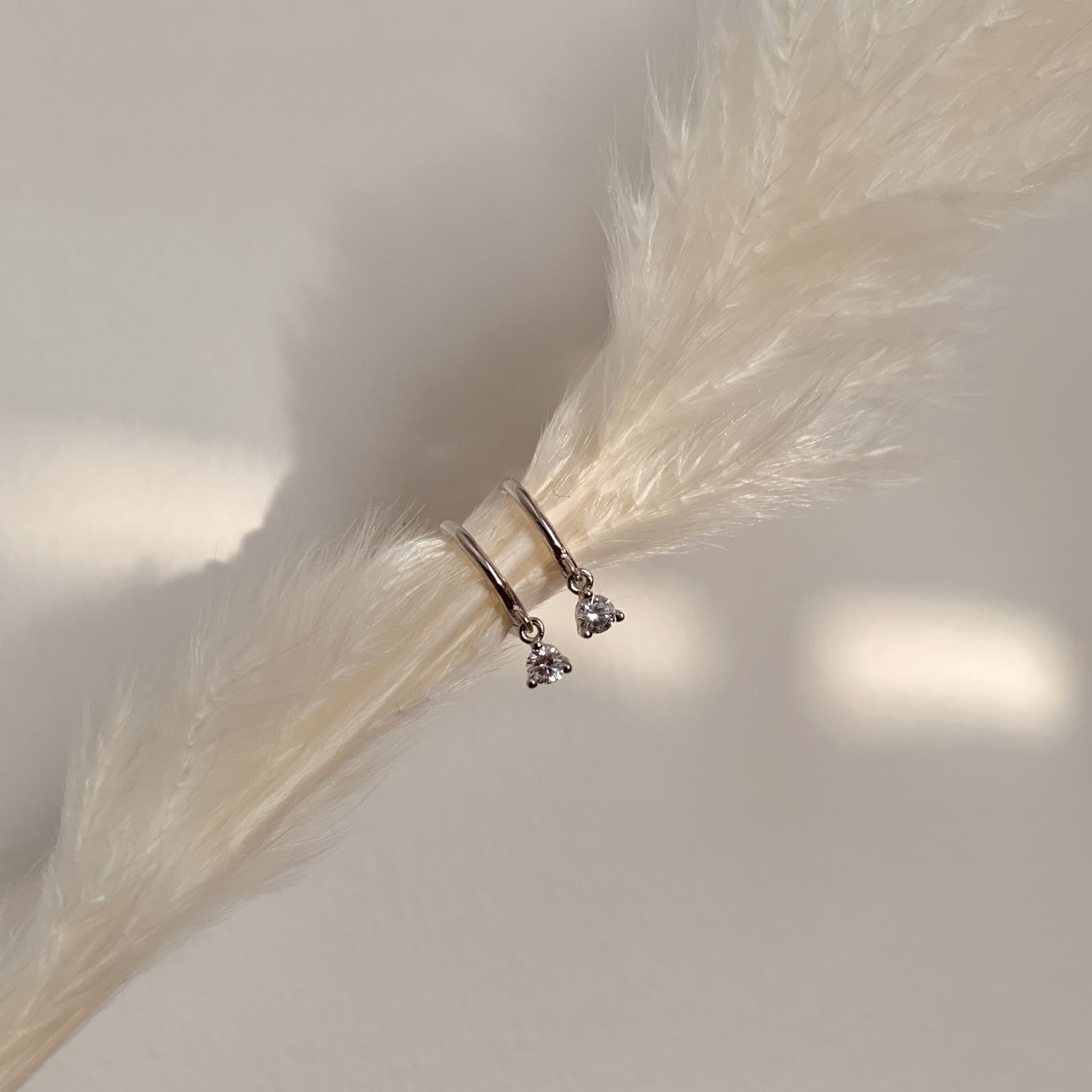 silver earrings with small dangling white zirconia charms, on a white feather