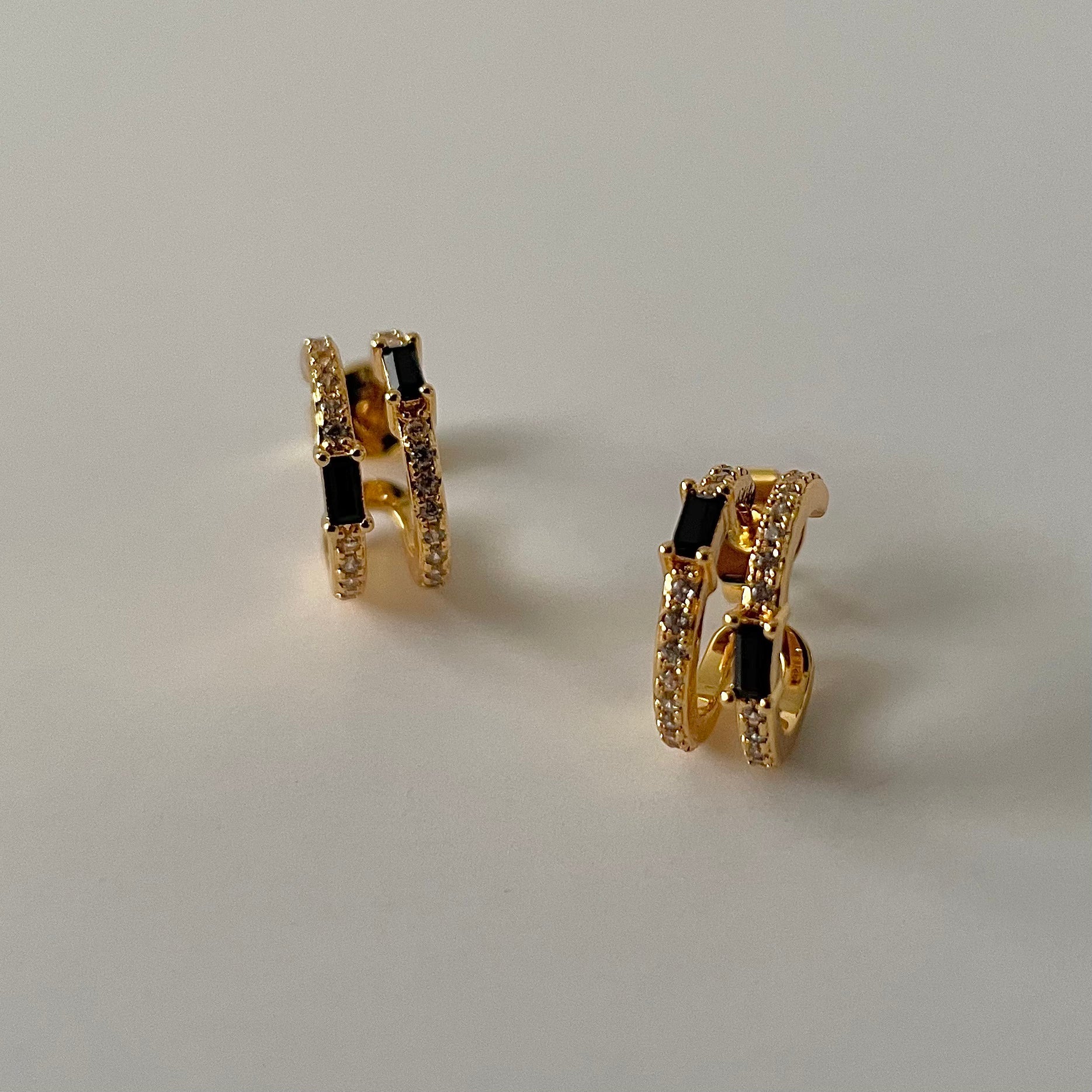 Gold hoop earrings with black stones and white zirconia crust on a light gray background