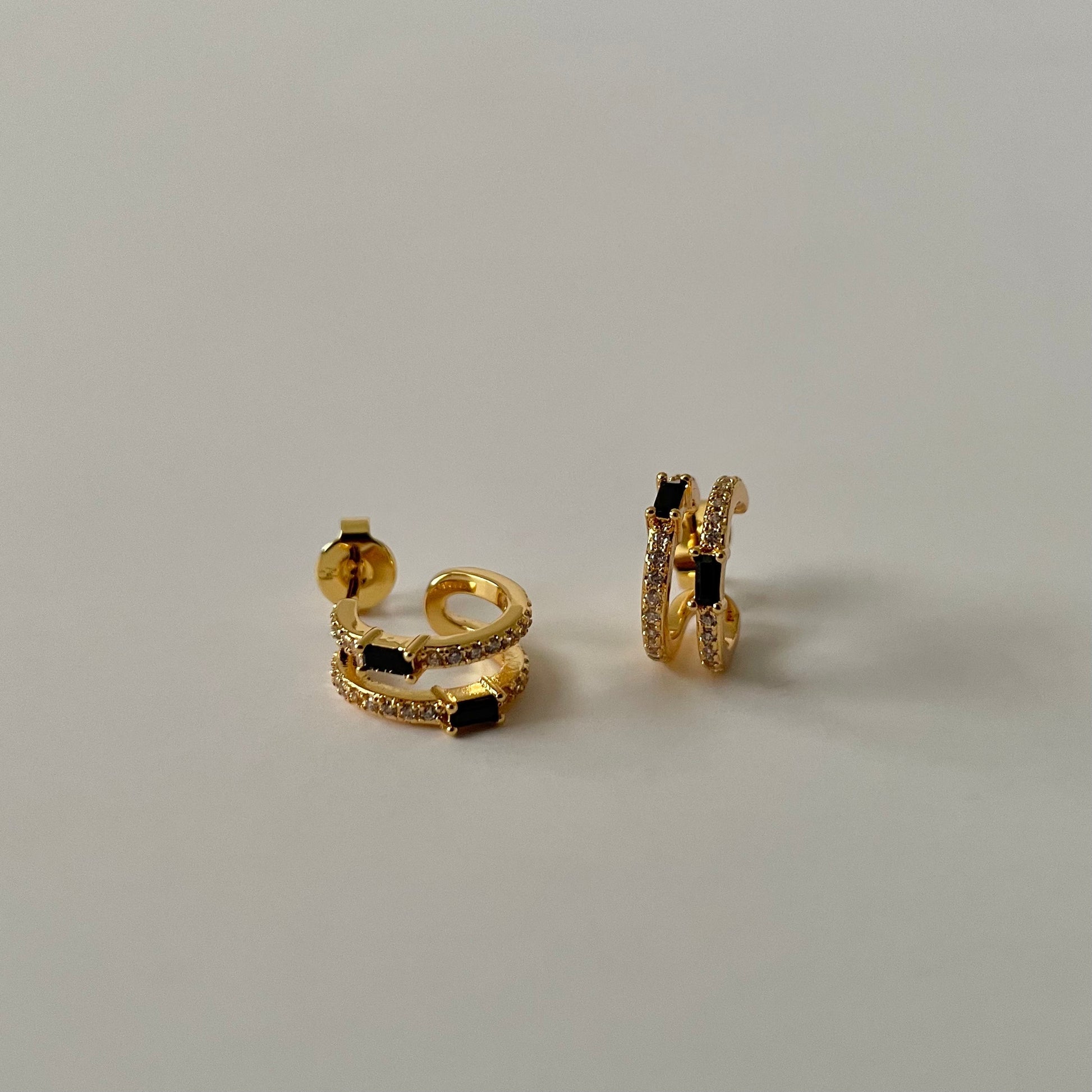 Gold hoop earrings with black rectangular stone and a white zirconia crust on a light gray background.