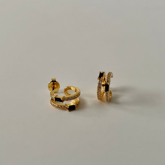 Gold hoop earrings with black rectangular stone and a white zirconia crust on a light gray background.