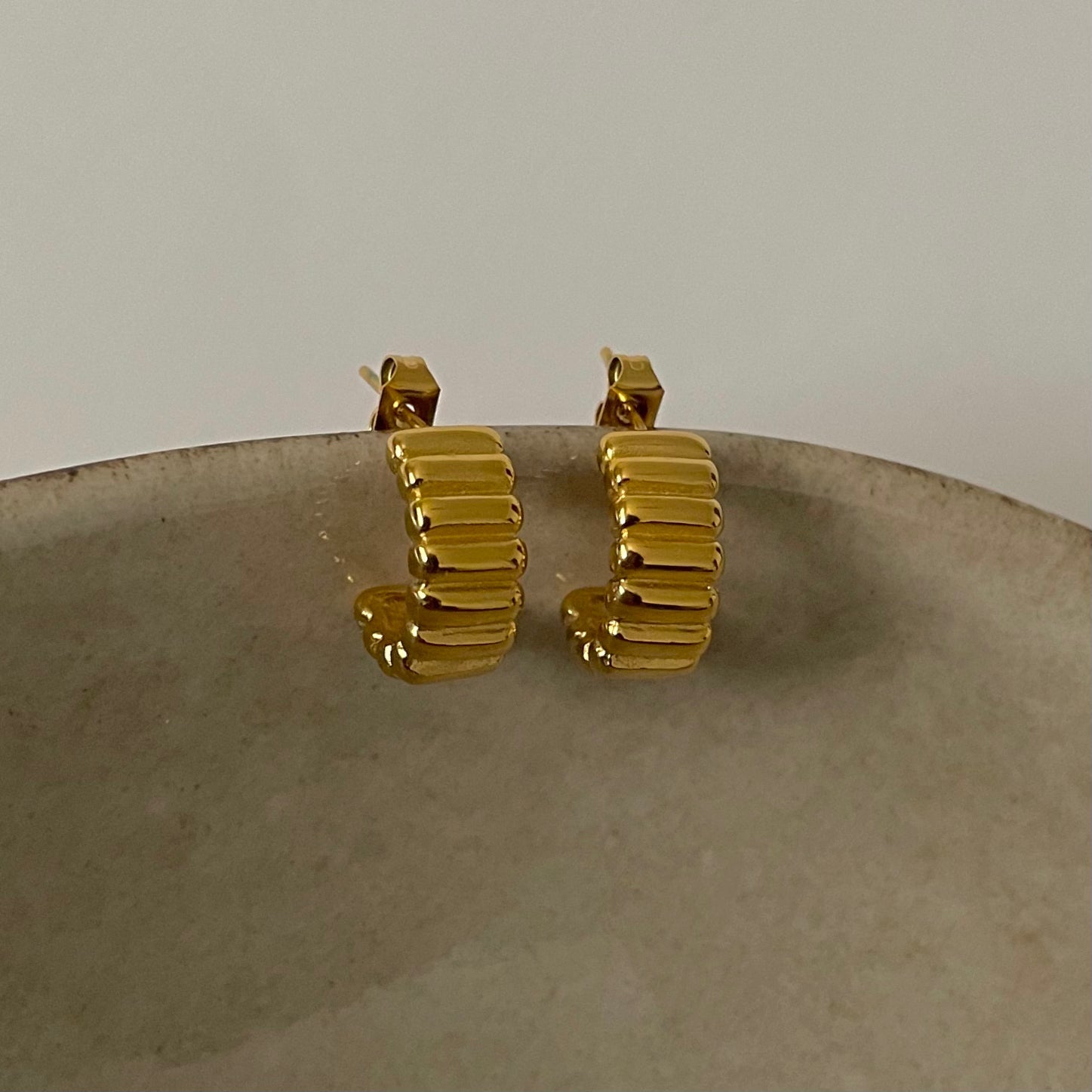 Gold ribbed hoop earrings on a textured surface with a neutral background