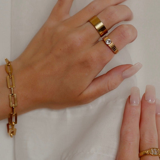 Hand wearing a gold bracelet and ring from daurielle on a plain background