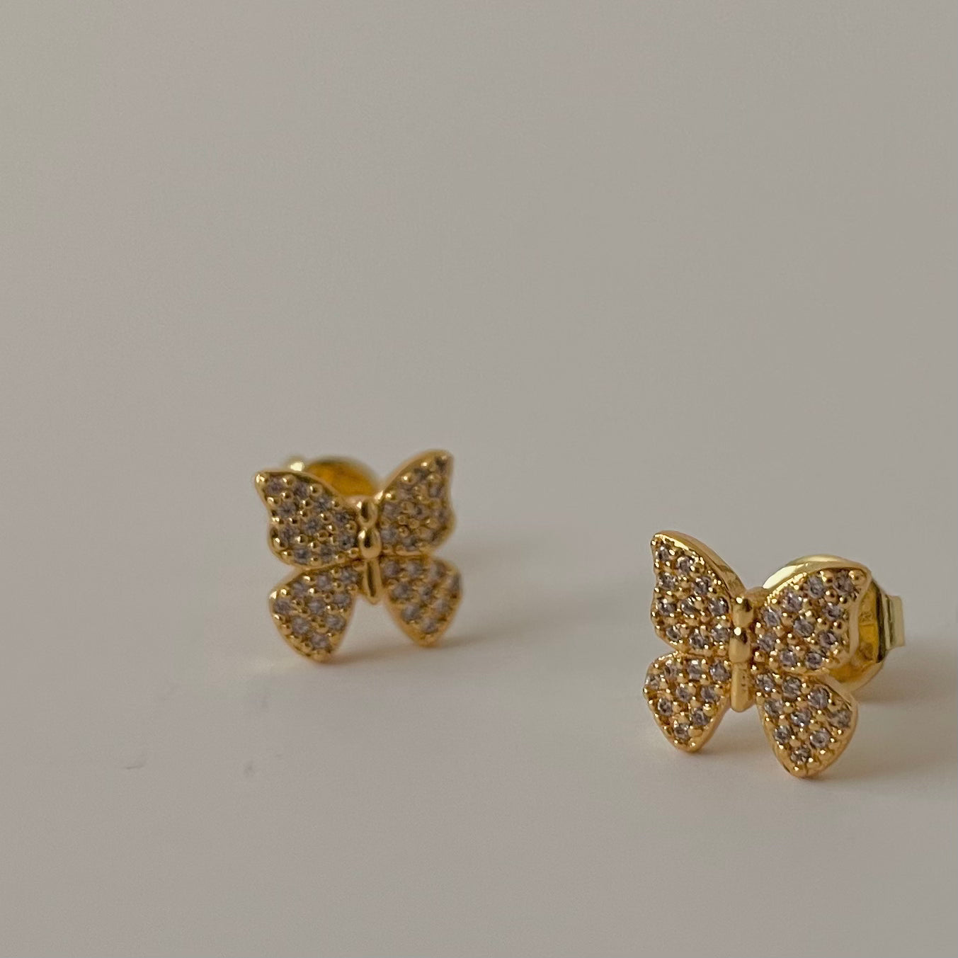 Gold butterfly earrings with gemstones on a light gray background