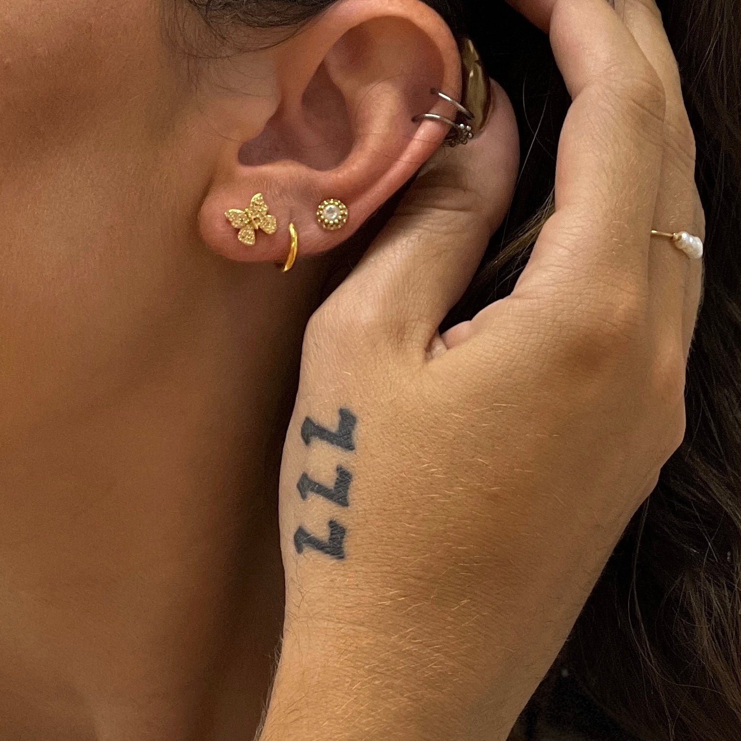 Close-up of an ear with gold earrings and a hand holding the ear, showing tattoos.