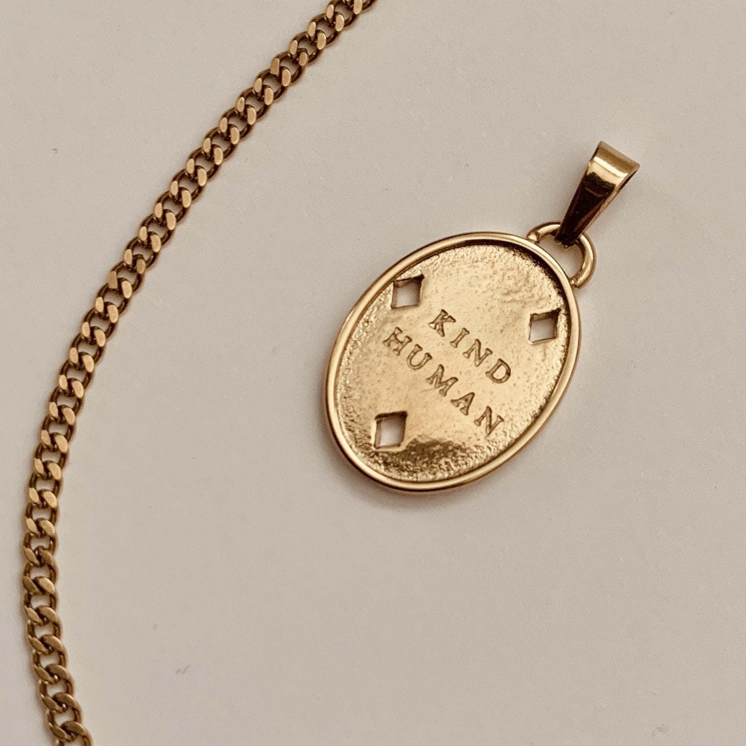 Gold necklace with a pendant that says 'Kind Human' on a light gray background