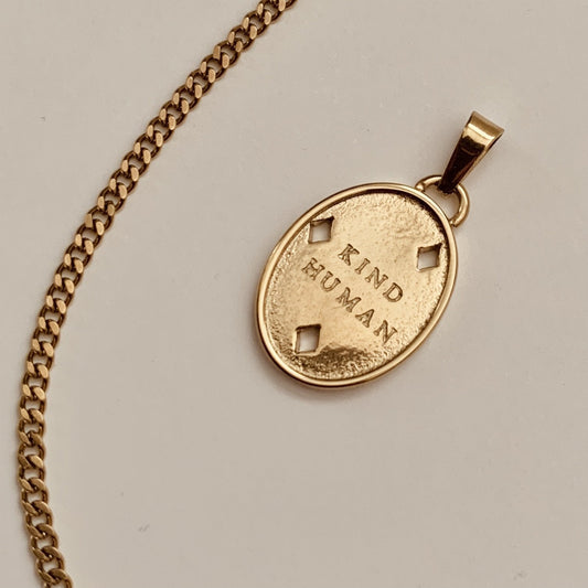 Gold necklace with a pendant that says 'Kind Human' on a light gray background