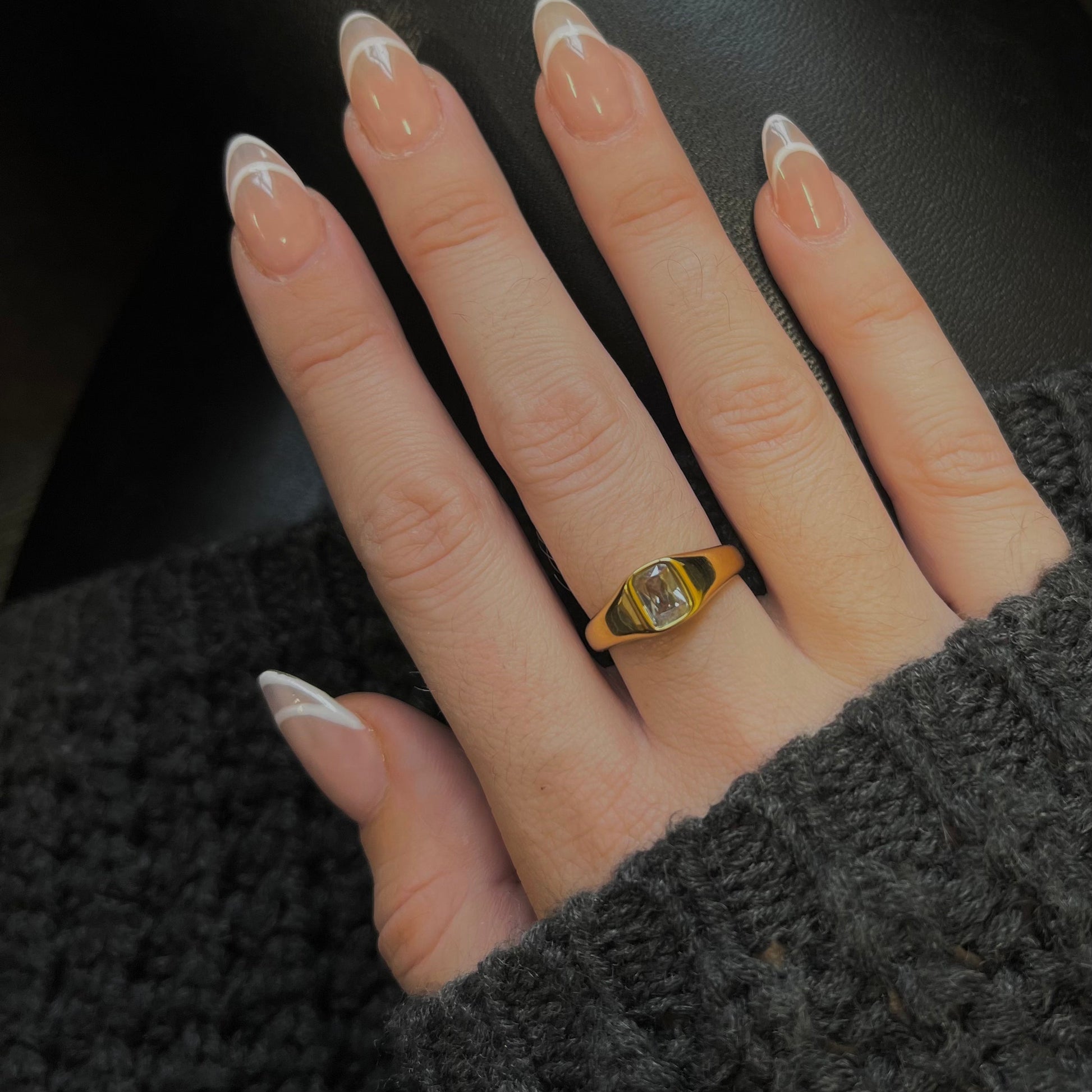Hand wearing a gold ring with a clear gemstone on a dark background