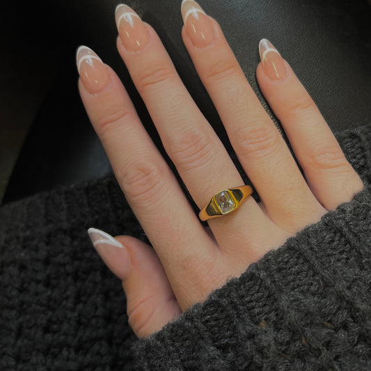 Hand wearing a gold ring with a clear gemstone on a dark background