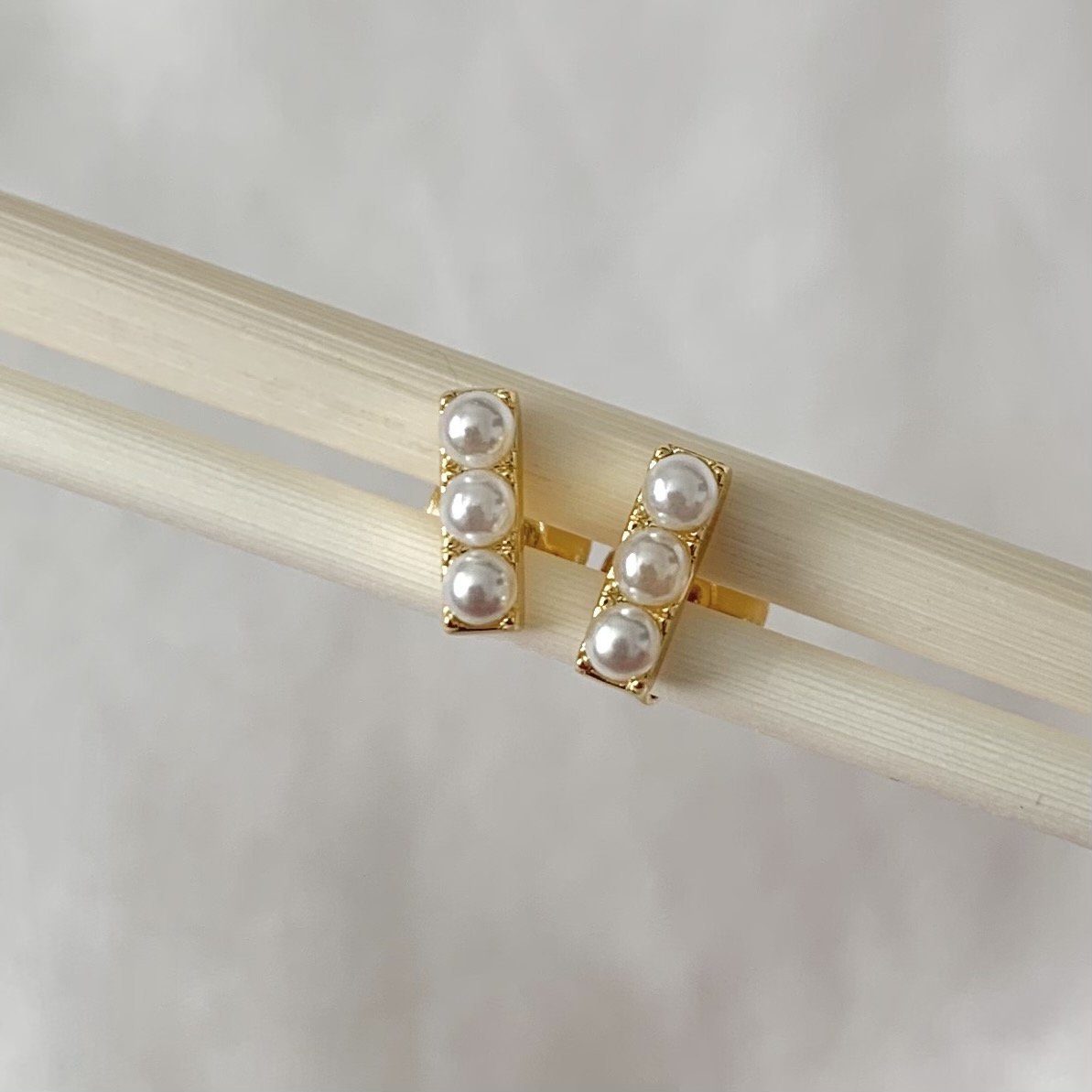 Pair of triple pearl earrings on a wooden stick with a plain background