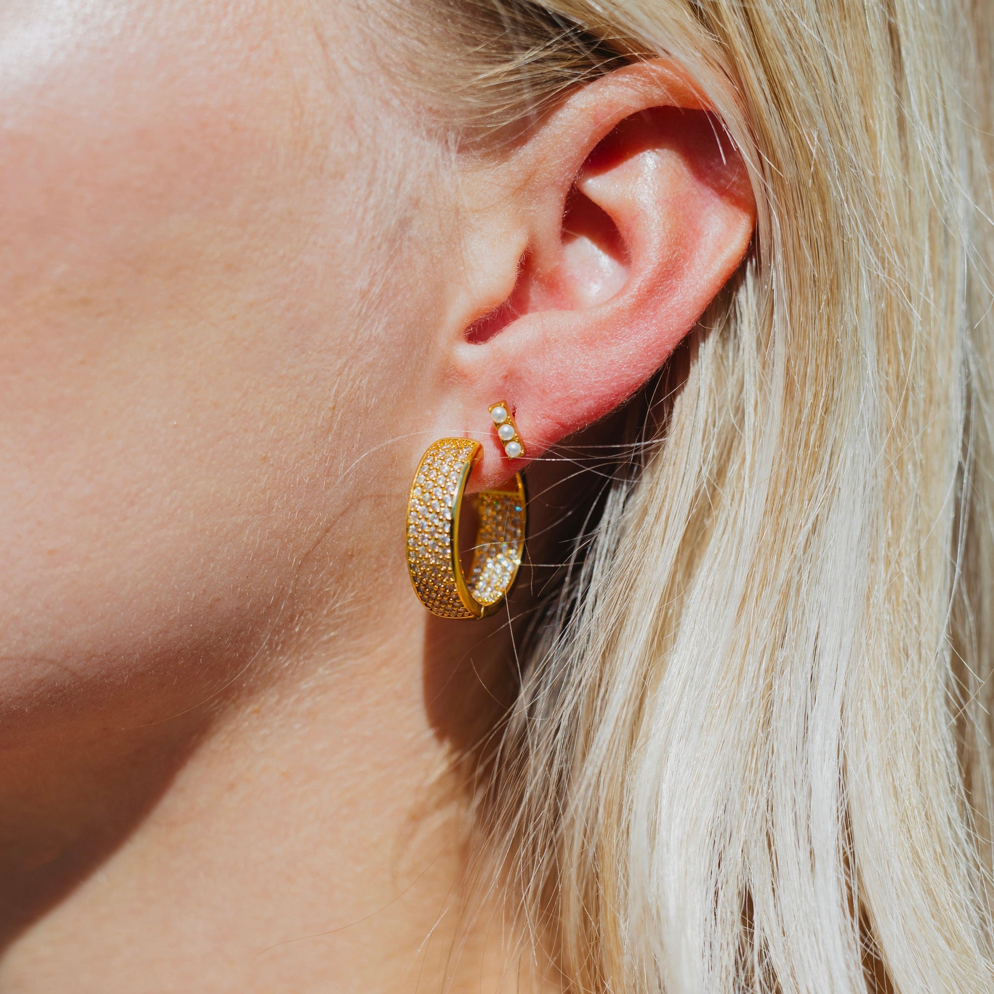 triple pearl stud earrings worn by a person with blonde hair.