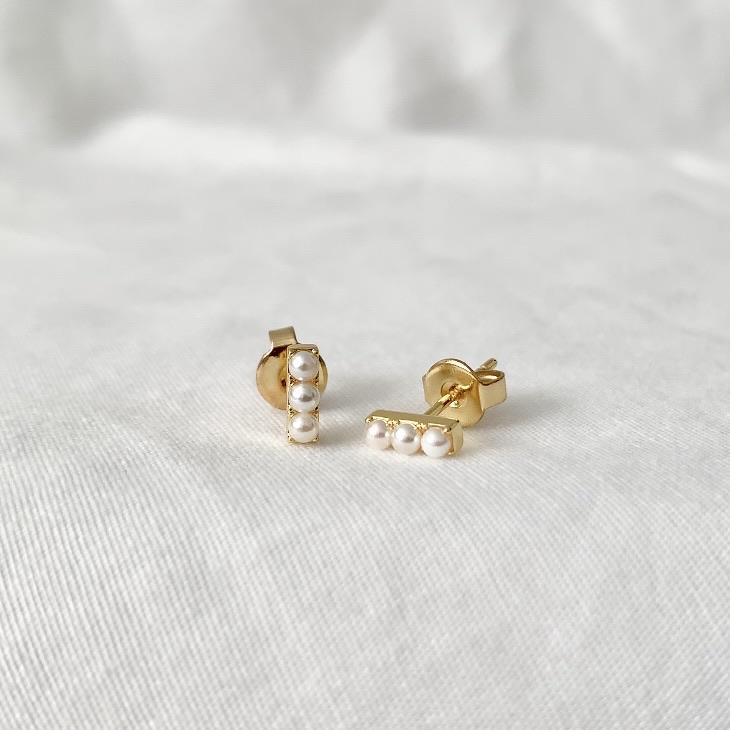 Gold earrings with 3 pearls on a white fabric background