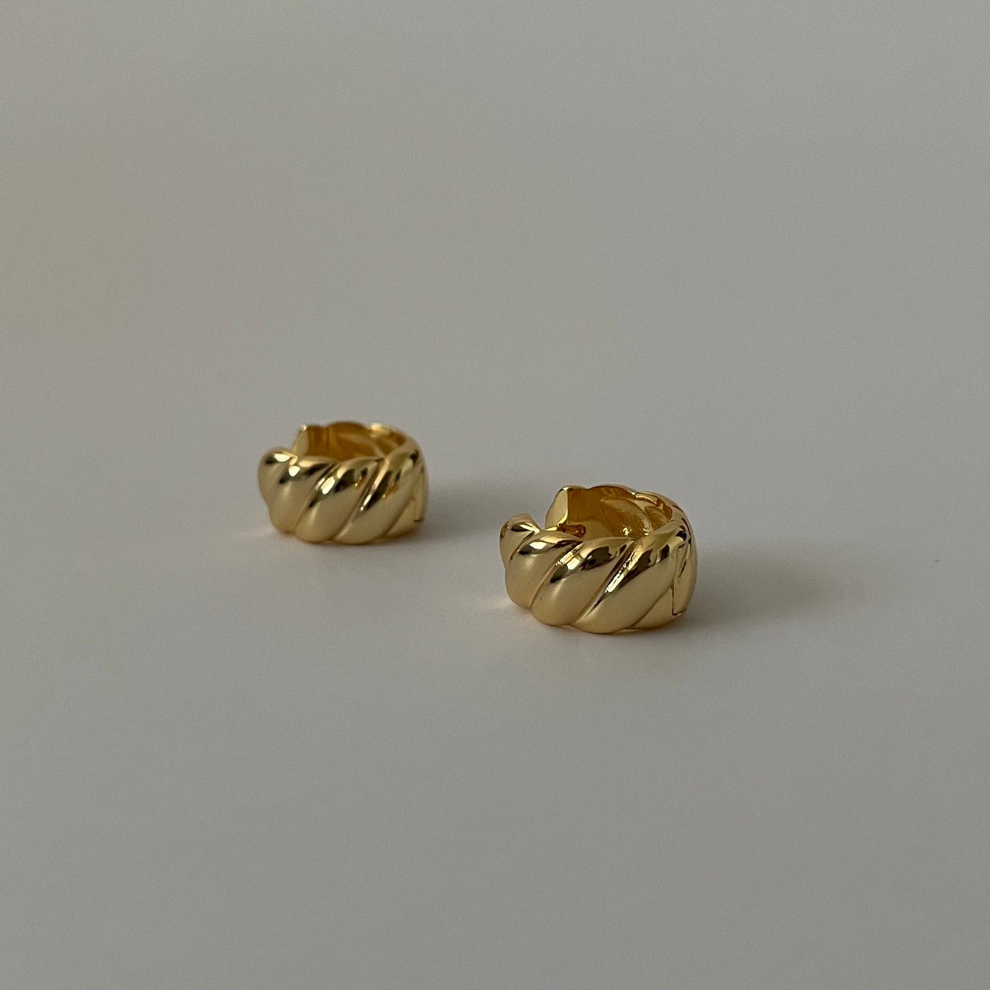 two gold sculptural huggie earrings on a plain grey background