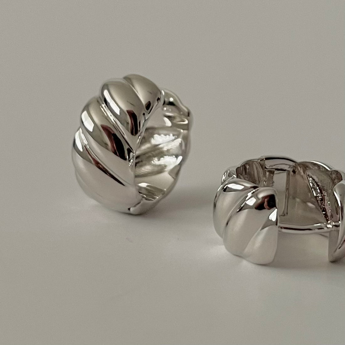 Pair of silver sculptural huggie hoop earrings on a light gray background.