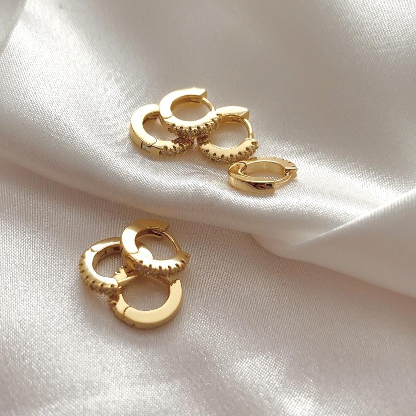 Gold hoop earrings with white zirconia crust on a soft white fabric background