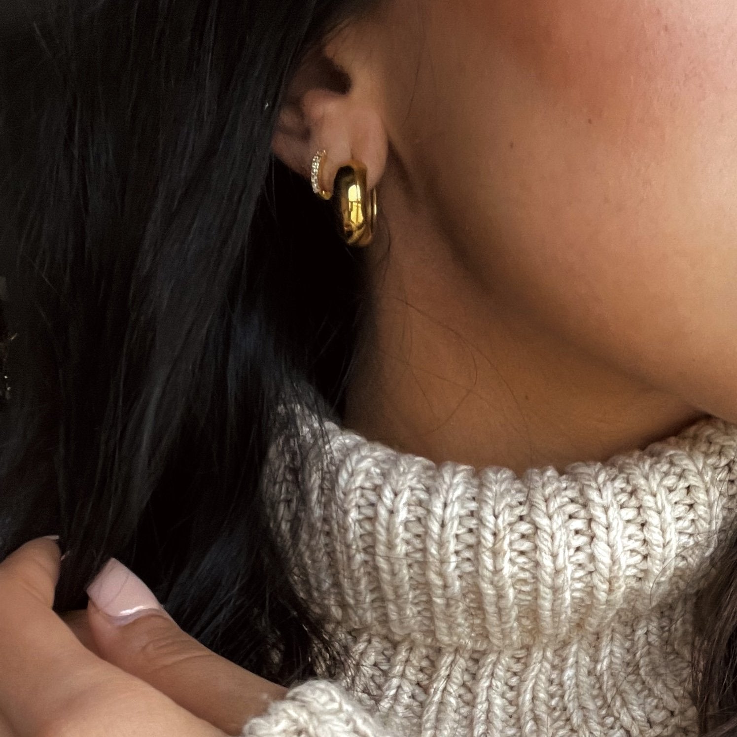 Close-up of a person wearing gold hoop earrings with white zirconia crust with a neutral background