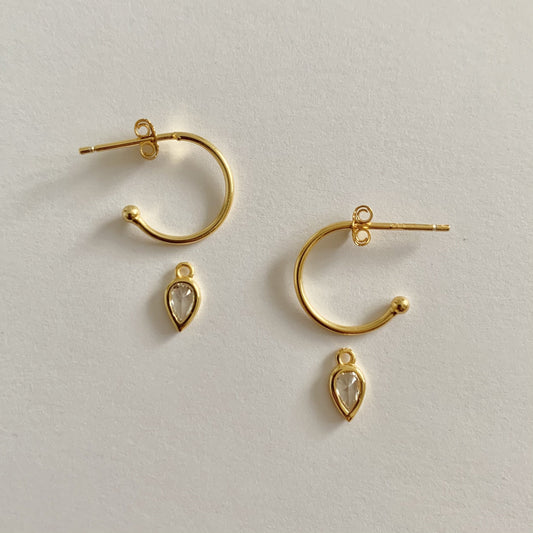Gold hoop earrings with teardrop-shaped charms on a light gray background
