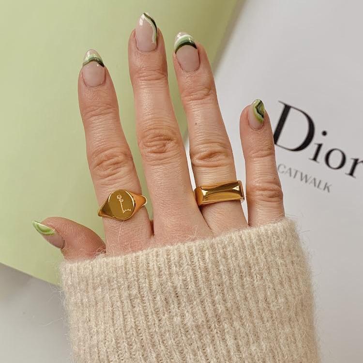 Hand wearing two gold rings with a Dior background