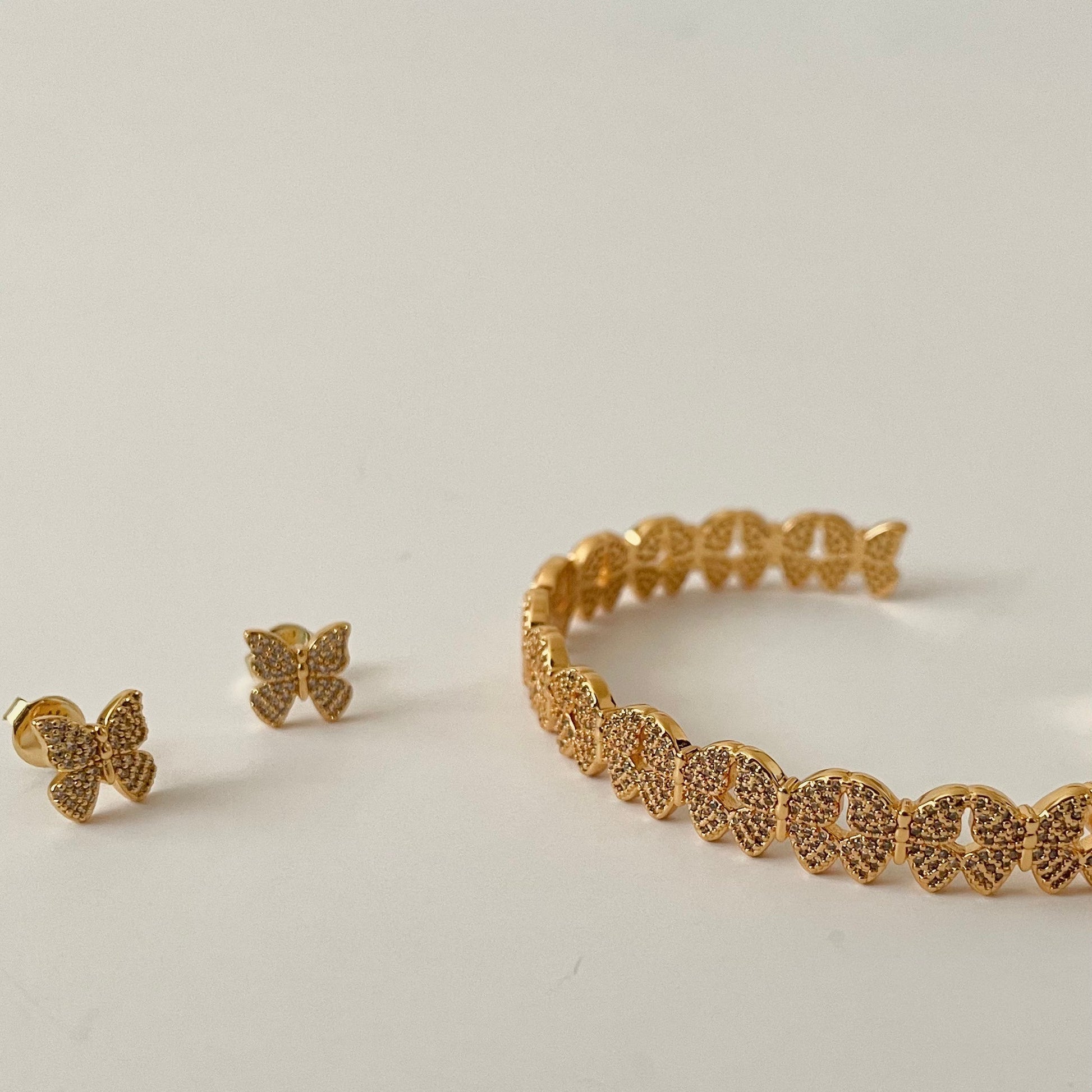 gold butterfly earrings with a pave finish next to a cuff bracelet made of the same design butterflies.