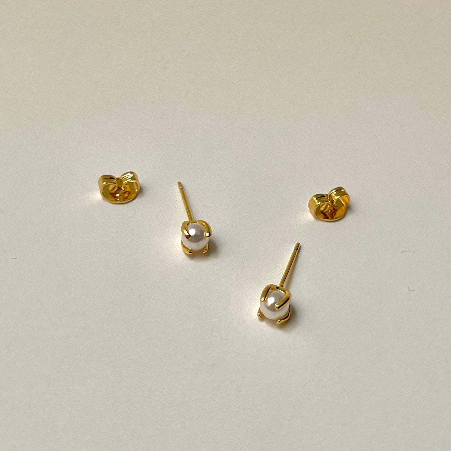 Gold stud earrings with a pearl center, light background
