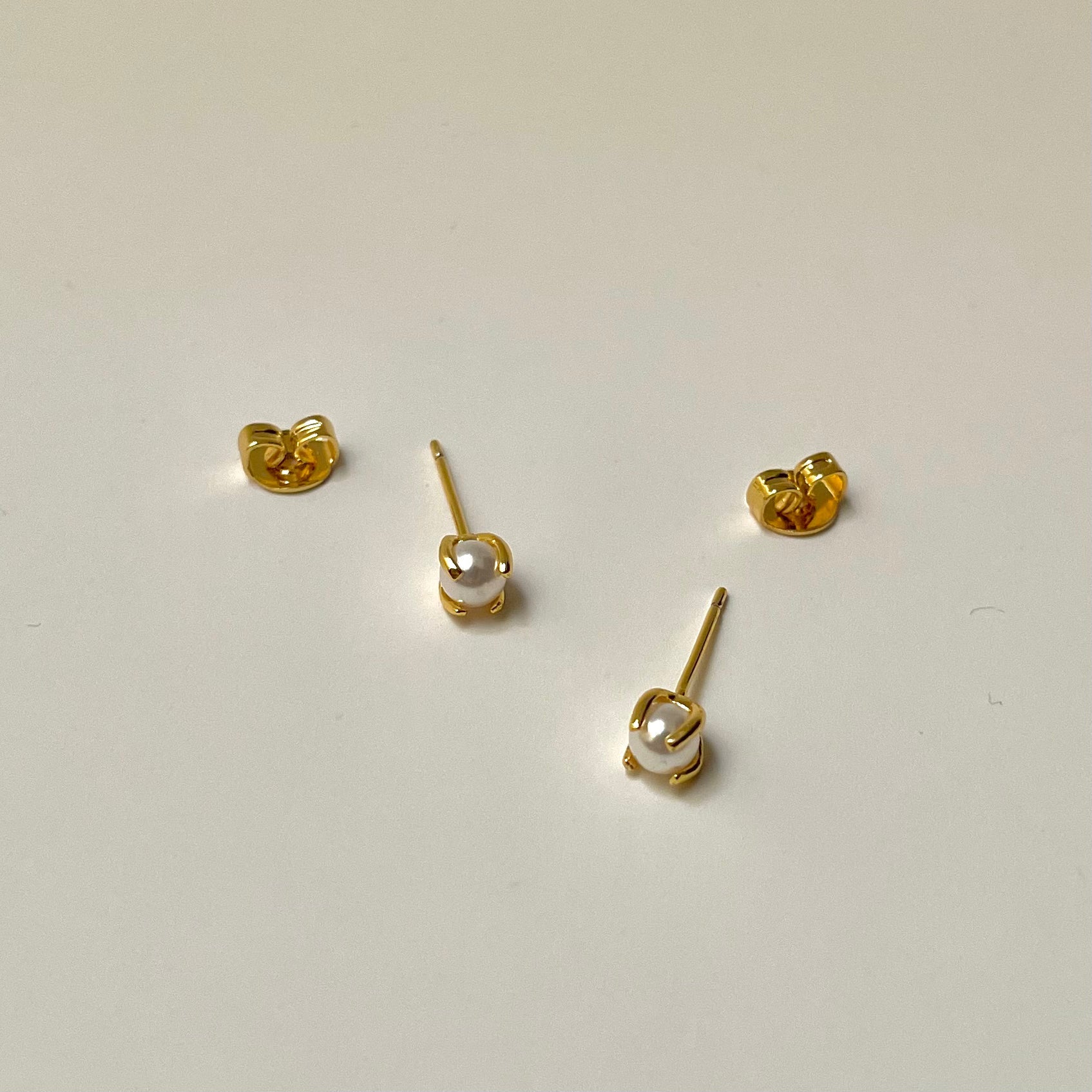 Gold stud earrings with a pearl center, light background