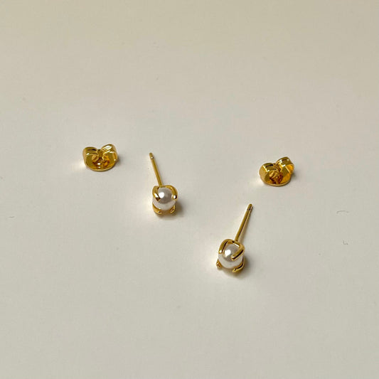 Gold stud earrings with a pearl center, light background
